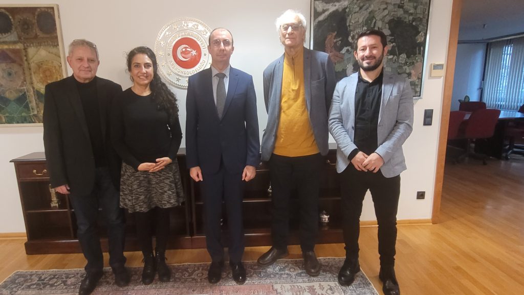 Das Bild zeigt fünf Personaen. In der Mitte steht Okan Şanlı, der Generalkonsul der Republik Türkei in einem Anzug. Links und rechts von Ihm stehen vier Vertreter:innen des TBB.