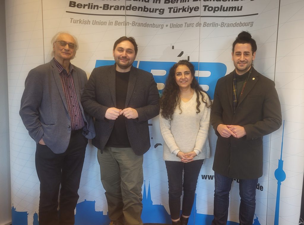 vier Personen stehen vor einem TBB-Logo mit schriftzug und lächeln in die Kamera. Von links nach rechts: Safter Çınar, Max Landero, Ayşe Demir und Orkan Özdemir